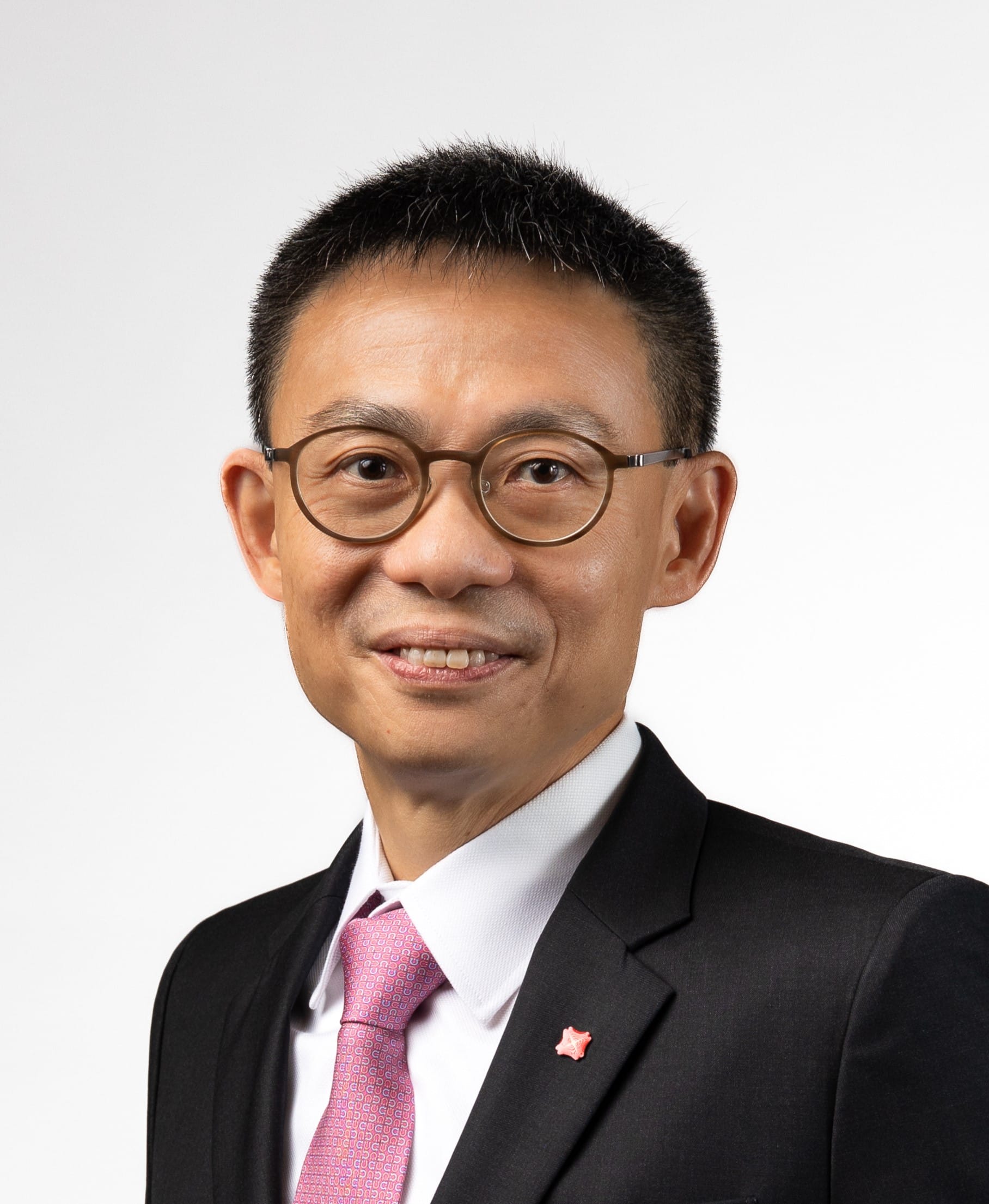 Man with glasses, wearing a black suit and pink tie, smiles.